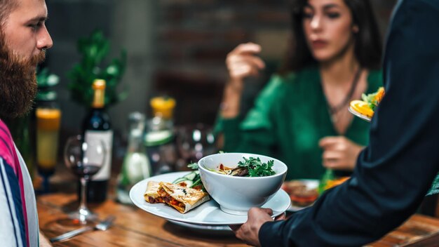 Horizontal image of male hand serving plate of vegetarian dinner in restaurant to a young couple