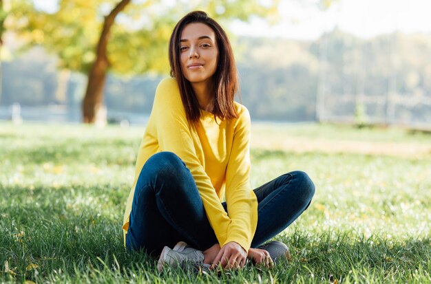 Horizontal image of a pretty happy young teenage girl relaxing outside in nature green park A pleasant happy young beautiful student female sitting outdoors in city park