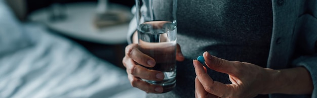 Horizontal image of t woman holding glass of water and pill