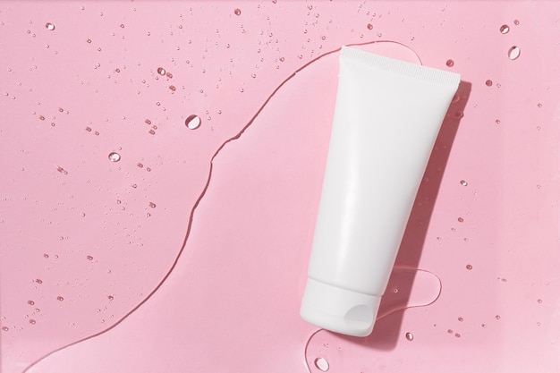 Horizontal image of white blank tube of face cream lying on textured water with bubbles on pink isolated background Natural cosmetics for skin care concept Image for your design or mockup