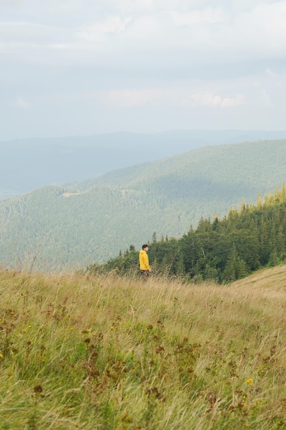 Horizontal image of a young man in a yellow jacket walking in a meadow with yellowed grass in the hi