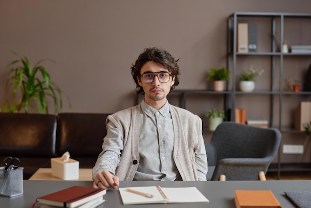 Horizontal medium portrait of young adult man working as psychologist sitting at desk in his office