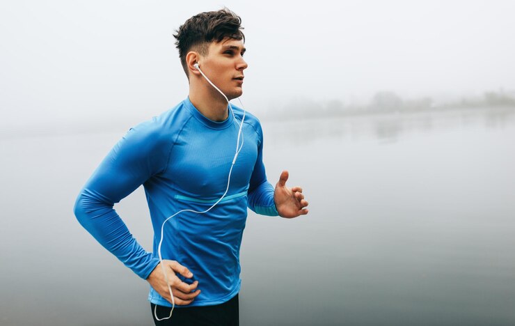 Photo horizontal outdoor image of young runner man running in the morning on the fog lake background fitness male exercising in the park and listenting the music on earphones people and sport concept