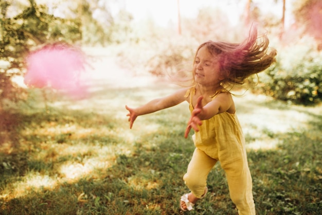 Horizontal outdoors image of beautiful little girl with long blonde hair playing in the park with magical pink dust for fairy tale concept Happy child dancing on her birthday party in the garden