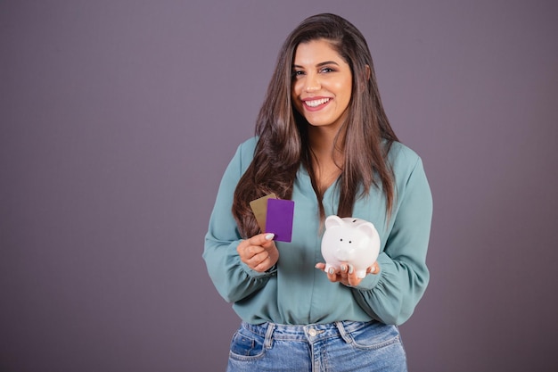 Horizontal photo Beautiful Brazilian woman with casual clothes Jeans and green shirt holding credit cards and piggy bank