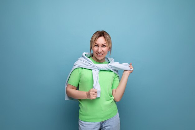 コピー付きの青色の背景にカジュアルな服装で金髪の肯定的な明るい女の子の横の写真