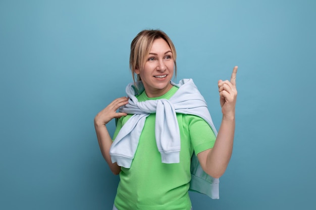 Foto orizzontale di una ragazza bionda positiva e brillante in un abito casual su sfondo blu con copia