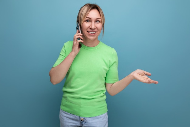 Horizontal photo of cheerful adorable blond woman with modern phone on blue background with copy