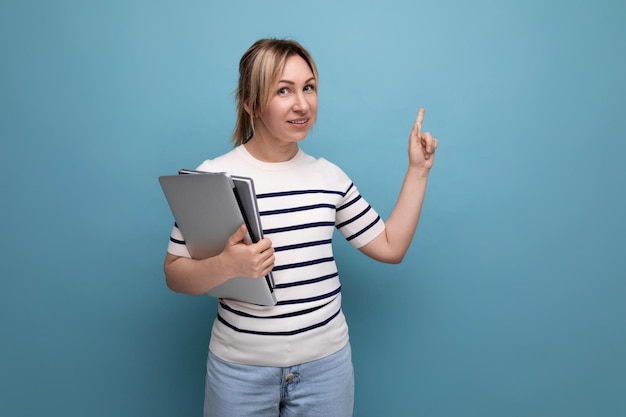 Horizontal photo of a confident blonde woman freelancer in a striped sweater holding a laptop in her