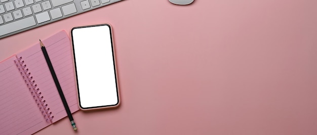 Horizontal photo of female workplace with smart phone notebook and copy space on pink background.