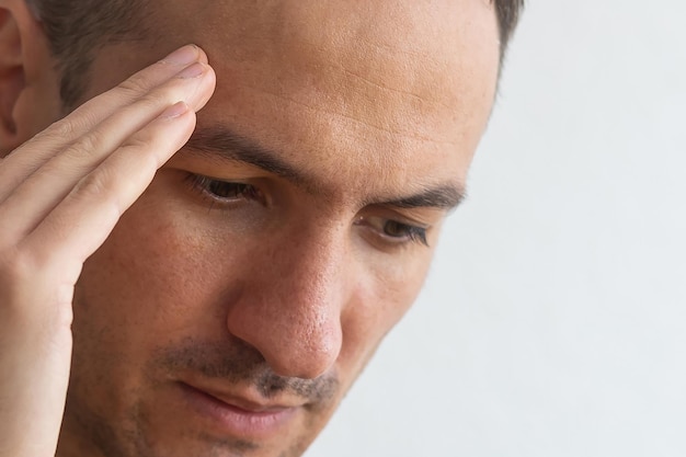 Horizontal photo of good-looking Caucasian man pictured isolated on gray background in right side of picture showing how much his head hurts, experiencing pain, looking miserable and exhausted