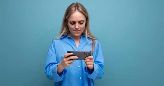 Horizontal photo of a lucky charming blonde girl holding a smartphone in her hands on an isolated