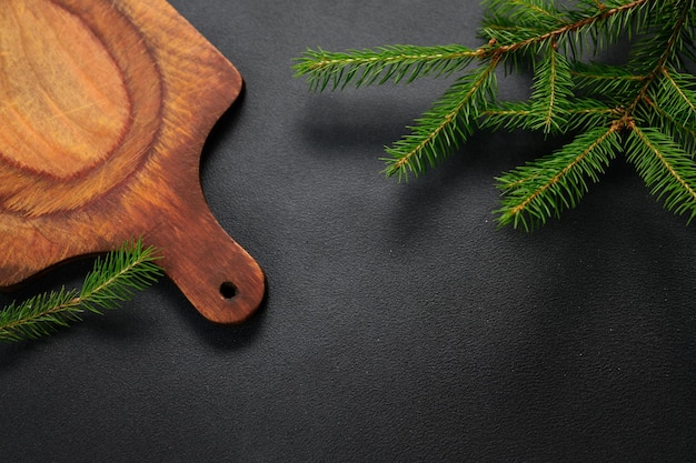 Horizontal photo Old cutting board with fir branches on dark background preparation for christmas