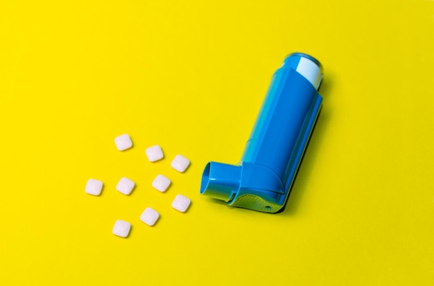 Horizontal photograph of a salbutamol inhaler with several pill adding asthma medicine on a yellow background Allergic diseases Copy space