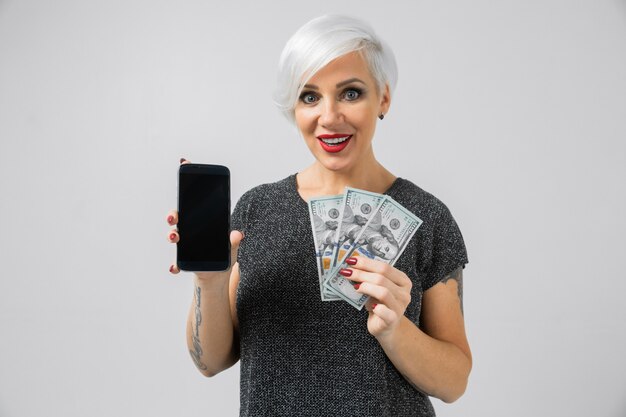 Horizontal portrait of adult blonde woman with smartphone and batch of money