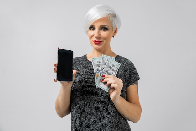 Horizontal portrait of adult blonde woman with smartphone and batch of money