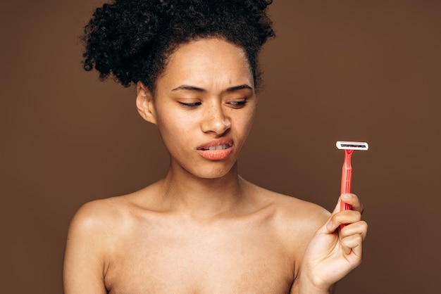 Horizontal portrait of beautiful sad woman with posing at the studio. Beauty fashion model woman with perfect skin and nude makeup holding razor and feeling disappointed