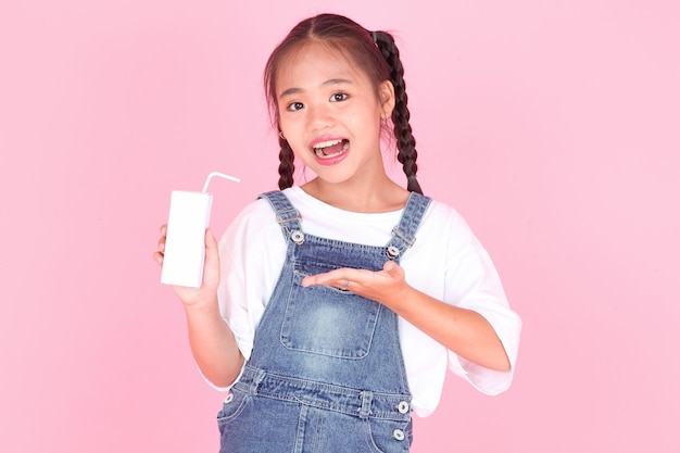 Горизонтальный портрет милой красивой азиатской маленькой девочки, держащей коробку с молоком на заднем плане