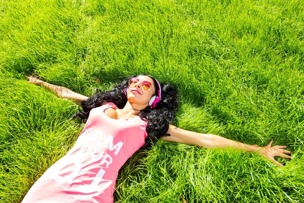 Horizontal portrait of pretty student girl spending day in park and showing thumb up Cheerful young female enjoying time in country Weekend and holiday concept