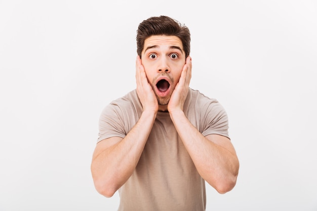 Horizontal portrait of scared man grabbing his face and screaming in stress, isolated over white wall