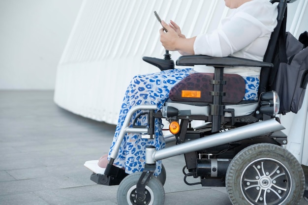 Horizontal portrait of an unrecognizable woman with disability in a wheelchair looking at her smartphone