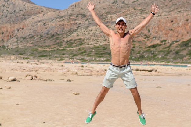 Горизонтальный портрет молодого человека на каникулах, счастливый скакать вверх на пляж. Copyspace