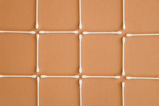 Horizontal rows of cotton swabs on beige background top view