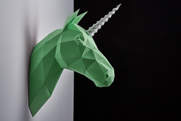 Horizontal shoot of green unicorn's head hanging on grey shadowed wall.