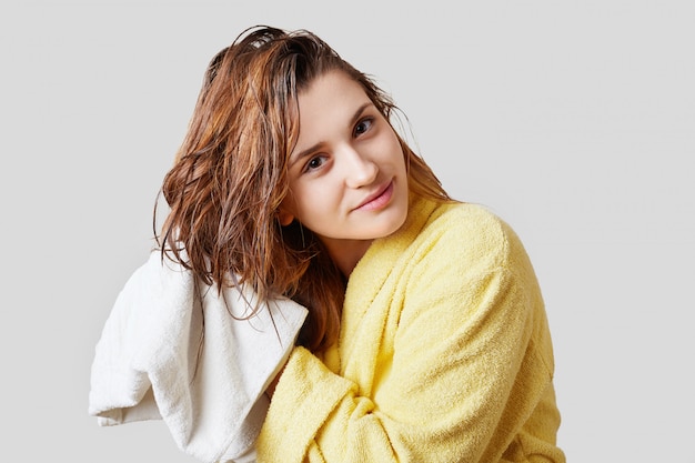 Horizontal shot of attractive female wipes wet hair with towel