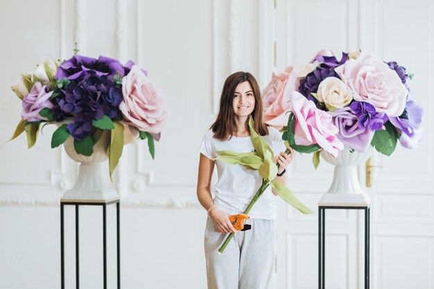 Horizontal shot of beautiful brunette young woman decorates hall for wedding holds garden forceps makes bouquets from artificial flowers likes designing People and floral designing concept
