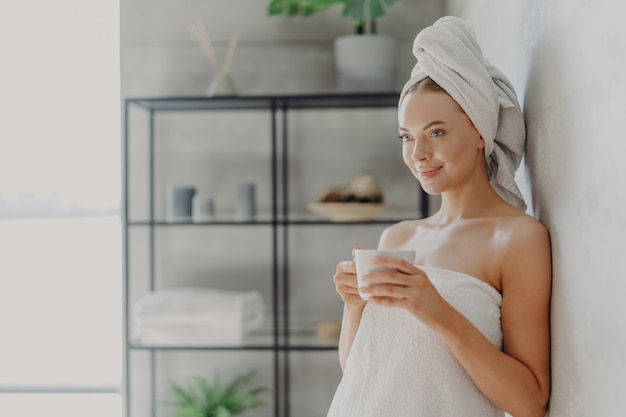 Horizontal shot of beautiful young woman with healthy skin wrapped in bath towel