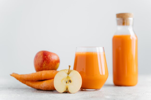 Colpo orizzontale di succo di carota detox in bottiglia e fetta di vetro di mela carota isolato su sfondo bianco bevanda naturale sana messa a fuoco selettiva