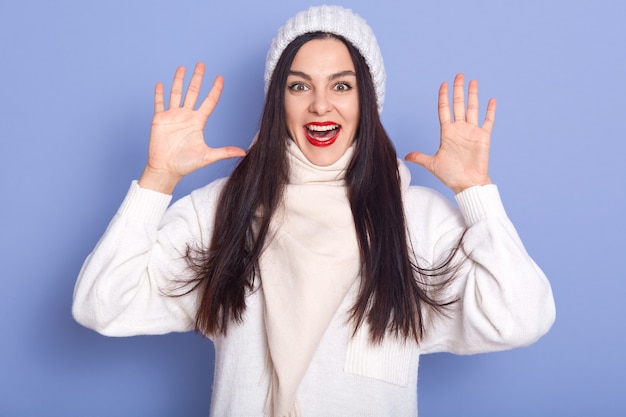 Horizontal shot of funny attractive brunette with red lips raising her hands