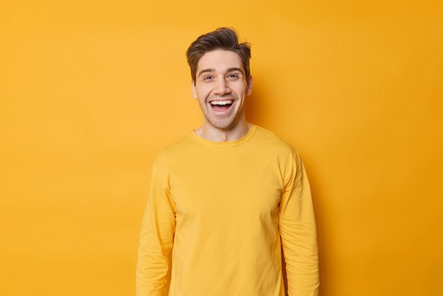 Horizontal shot of happy young european man laughs joyfully expresses positive emotions dressed in casual jumper isolated over vivid yellow background monochrome shot positive guy indoors