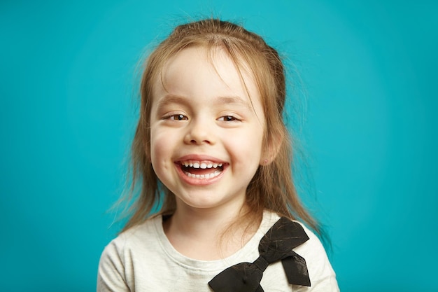 Horizontal shot of joyful kid girl with charming smile sincerely laughs expresses cheerful mood and pleasure emotional children portrait over blue isolated background