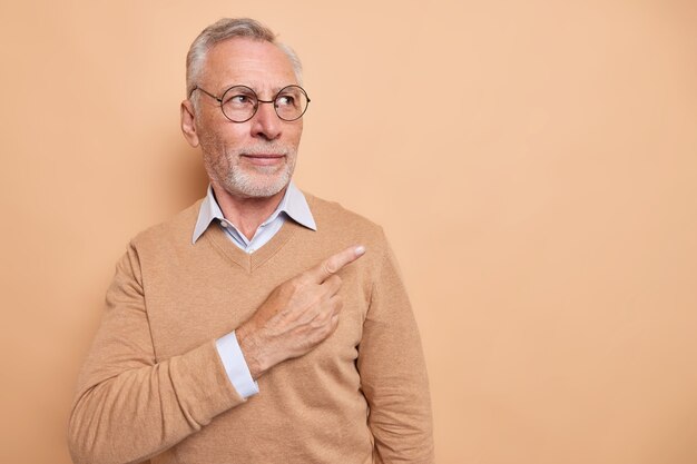 Horizontal shot of serious bearded elderly man points at upper right corner