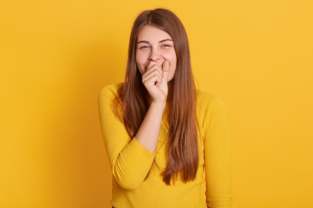 Horizontal shot of young attractive Caucasian female standing against yellow wall