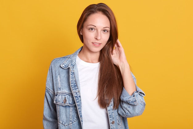 Horizontal shot of young charming woman in denim jacket and white casual shirt