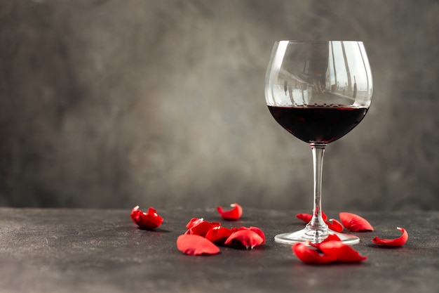 Horizontal side view on a glass of red wine on the table decorated with petals