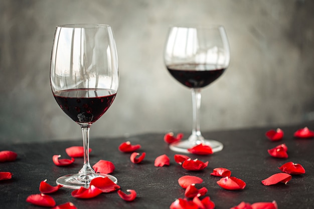 Horizontal side view on a glasses of red wine on the table decorated with petals