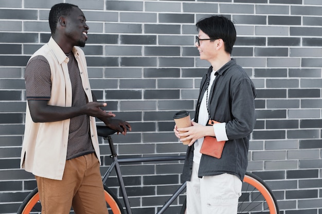 Horizontal side view shot of handsome African American guy and stylish Asian woman standing together outdoors enjoying conversation