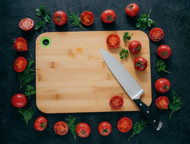 Photo horizontal top view of red tomatoes lying around wooden chopping board.