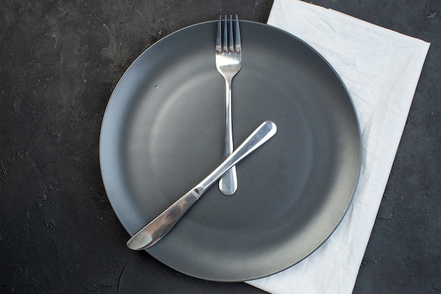 Horizontal view of cutlery set on a black plate on white towel on dark color background with free space