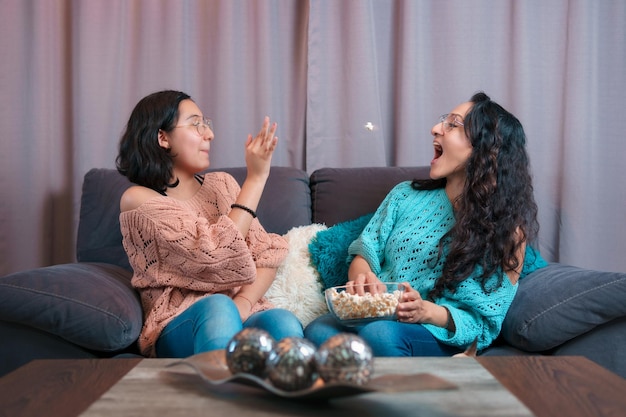 Horizontal view of a mom and her daughter watching a movie at\
home they play throwing popcorn to catch it with their mouths they\
make very funny expressions