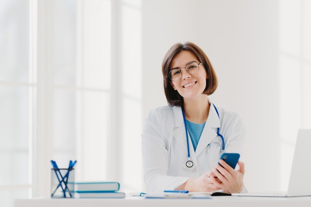 Фото Горизонтальный вид улыбающегося профессионального врача работает в клинике, позирует в современном офисе больницы с электронными устройствами