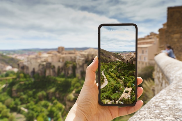 Foto vista orizzontale di una donna irriconoscibile che scatta una foto con il suo telefono di una destinazione di viaggio in europa. concetto di tecnologia, turismo e vacanze nella città spagnola di cuenca.