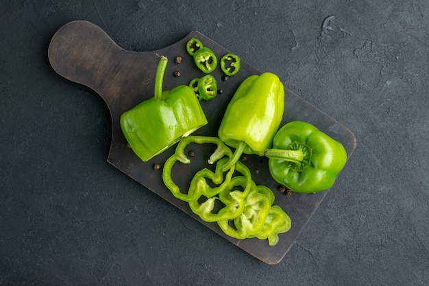 Horizontal view of whole cut chopped green peppers on dark color wooden cutting board on black surface