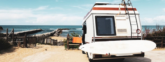 Horizontale banner of kop met achteraanzicht van vintage camper geparkeerd op het strand tegen een schilderachtig uitzicht Caravan van surfer met een surfplank op de rug Nomadisch en van levensconcept