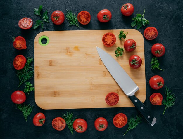 Foto horizontale bovenaanzicht van rode tomaten die rond houten hakbord liggen.