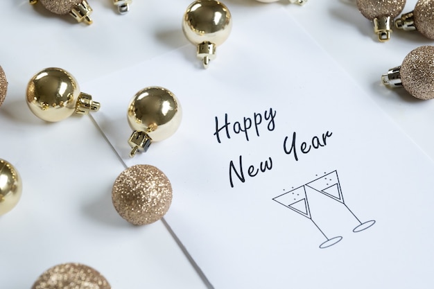 Horizontale close-up van "gelukkig nieuwjaar" kaart omringd door gouden kerstballen, witte achtergrond en kopieer ruimte.